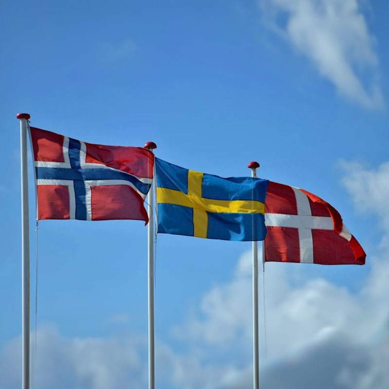 Tre flaggstänger med norge, sverige och danmarks flagga.